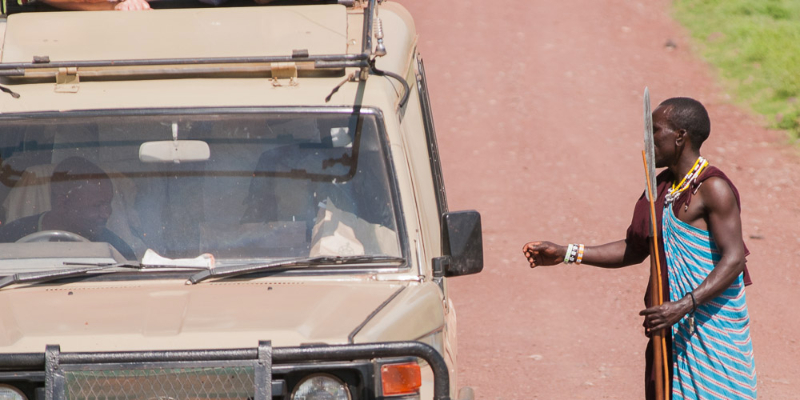 un massaï demande de l'argent à une voiture de safari